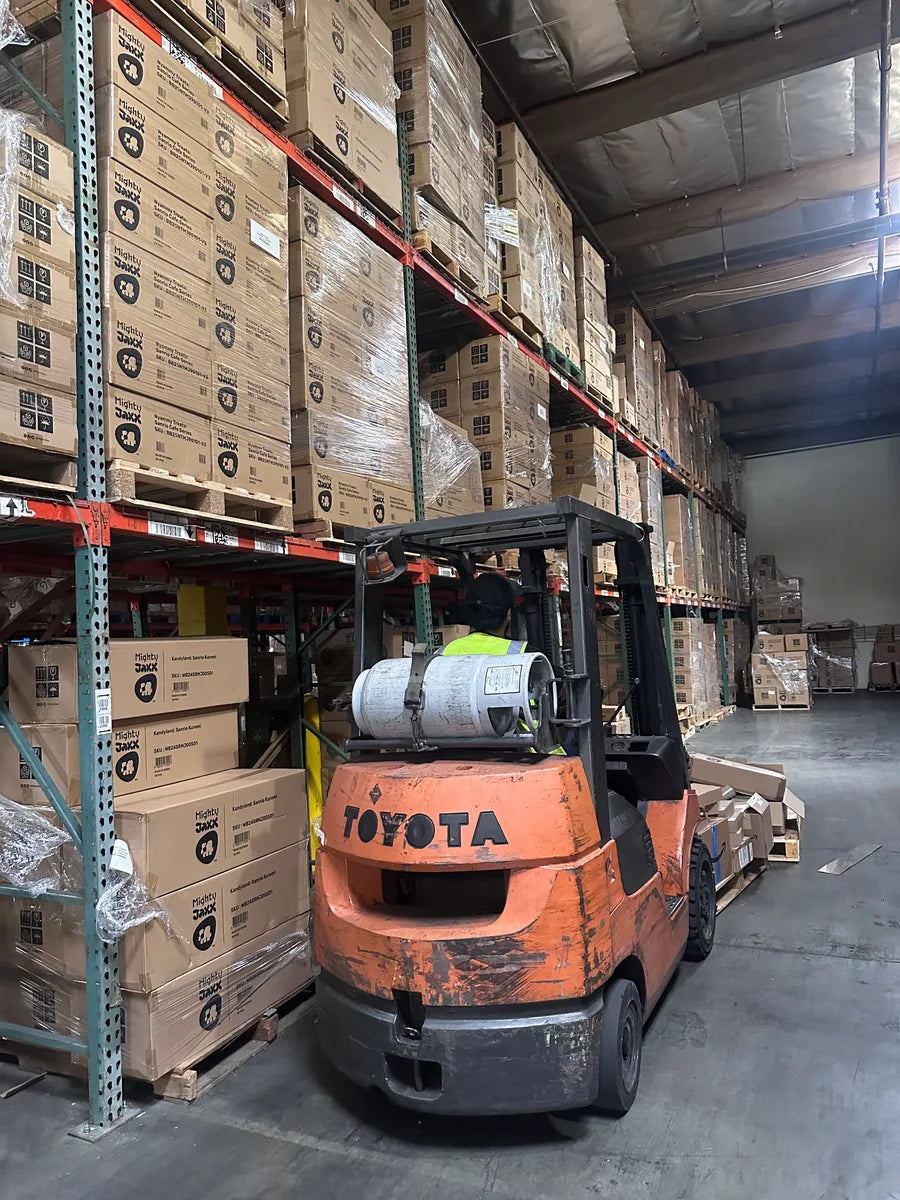 Warehouse aisle with pallet racking, cartons, and a forklift in operation