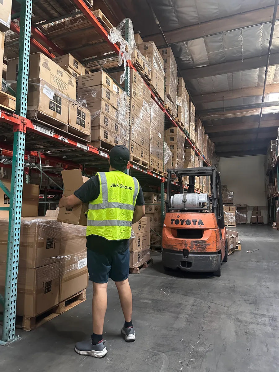 Warehouse staff member handling a carton beside pallet racking and a forklift